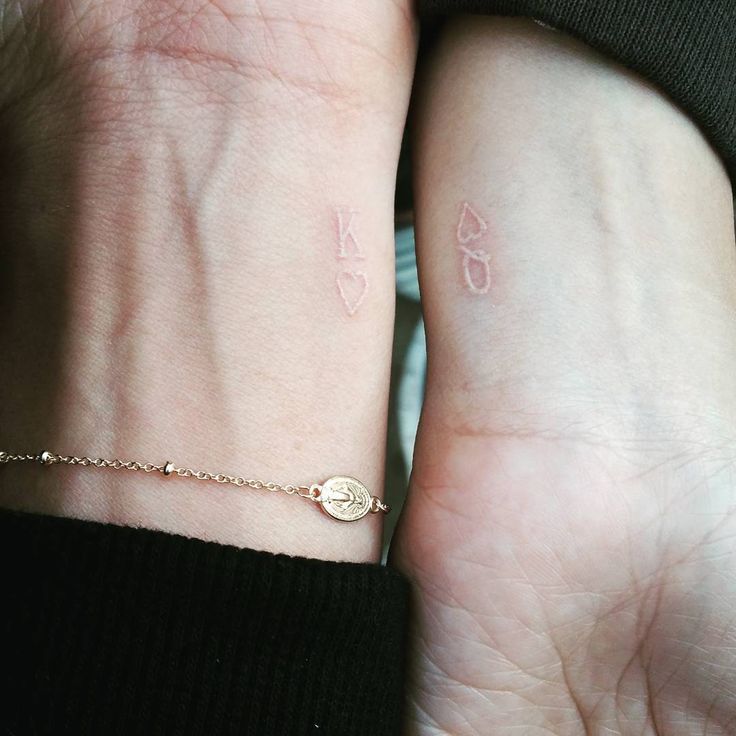 two people holding hands with tattoos on their wrist and one has a small heart tattoo