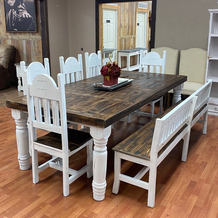 a wooden table with white chairs and a bowl of flowers on it in front of a mirror