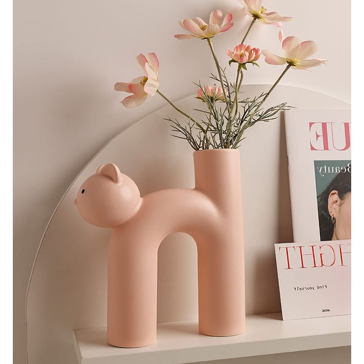 a pink vase with flowers in it sitting on a shelf next to a magazine rack