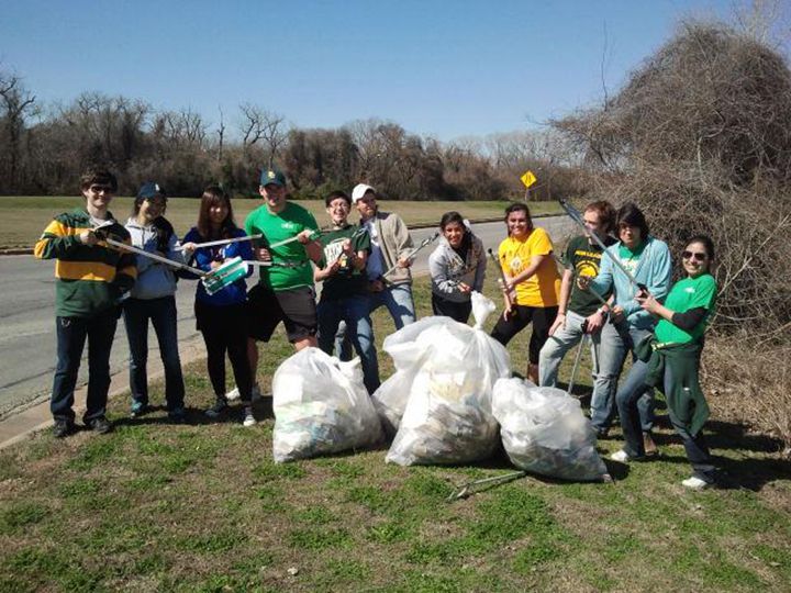 a group of people standing next to each other holding bags and shovels in the grass