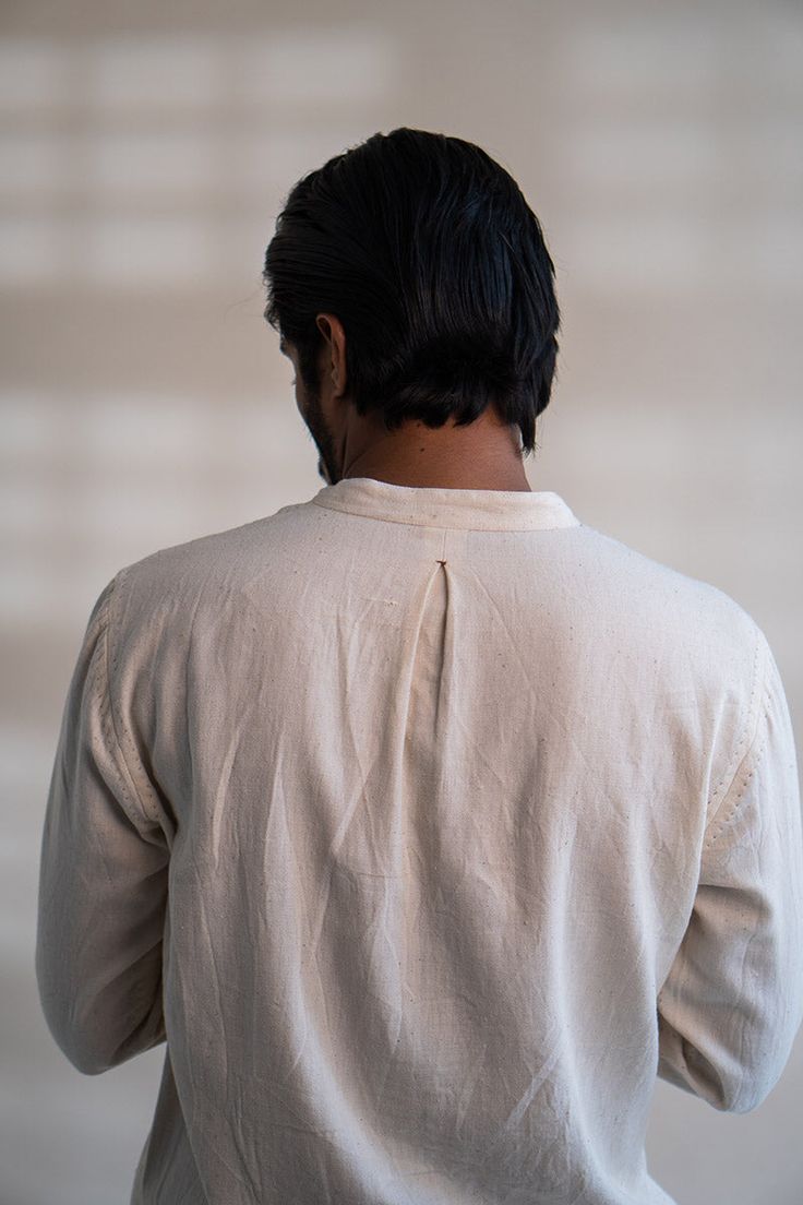 100% Cotton • Hand Spun • Hand Woven • Undyed • Unbleached • Embroidery DetailThis Dawning Panelled Long Shirt comes in a calm and soothing colour that we call Kora. Crafted in 100% cotton fibres and natural materials. This Kala Cotton shirt is undyed and unbleached. It has a band collar and full front panelling. This full-sleeve shirt comes with two patch pockets that are extensively adorned with stitches of Kantha, a form of Indian hand embroidery.Type of Button used: Coconut Shell Buttons Indian Hand Embroidery, Slow Clothing, Kantha Embroidery, Soothing Colors, Band Collar, Sustainable Clothing, Long Shirt, Traditional Techniques, Hand Spinning