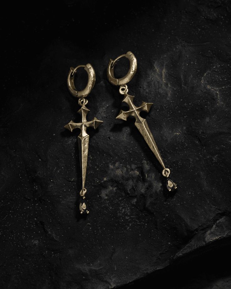 A blade of cryptic provenance drips ebony beads, having paid witness to magick’s wicked creeds. Sword earrings with hilts forming pointed gothic crosses - the symbol in our Ask & Embla logomark. At the point of each sword hangs a black crystal gem. Ear posts made from 925 Silver - kinder to sensitive skin. Sold as a pair. Each piece is lovingly crafted by hand, under ethical working conditions. Please allow for minor imperfections that are true to handcrafted jewelry. No two pieces are the same Afro Jewelry, Gothic Crosses, Dragon Earrings, Studs Earrings, Online Jewelry Store, Black Crystals, Crystal Gems, Ear Studs, Black Beads