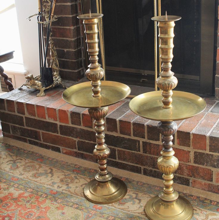 two brass candlesticks sitting in front of a fireplace