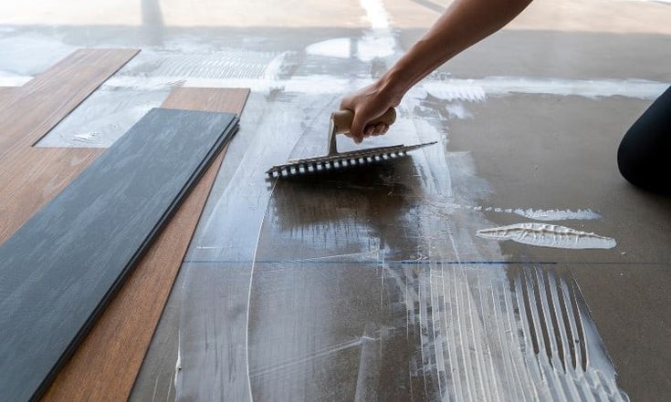 a person with a brush laying on the floor next to some tiles and wood planks