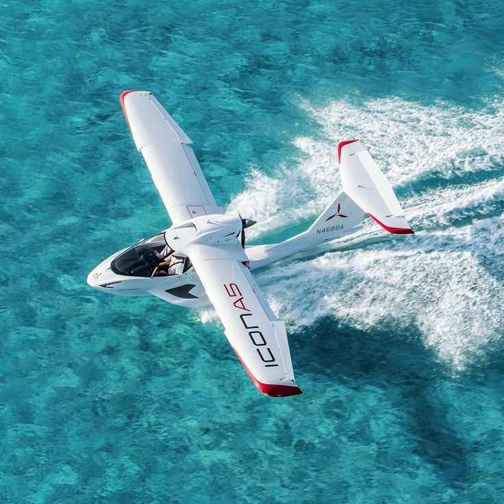 an aerial view of a small airplane flying over the blue water in the ocean with its landing gear down