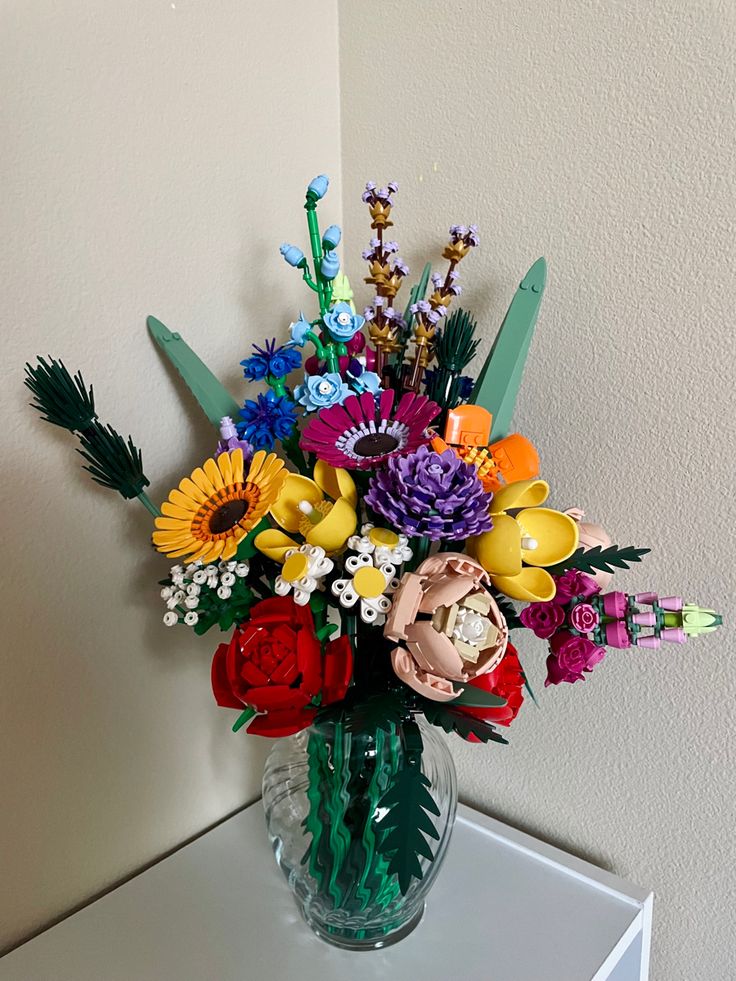 a glass vase filled with colorful flowers on top of a white table next to a wall