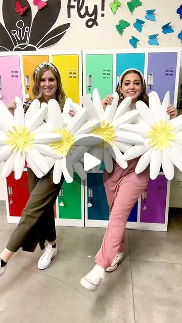 two girls are holding giant paper flowers in front of lockers