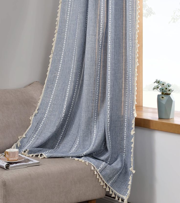 a blue curtain hanging from a window next to a couch with a book on it