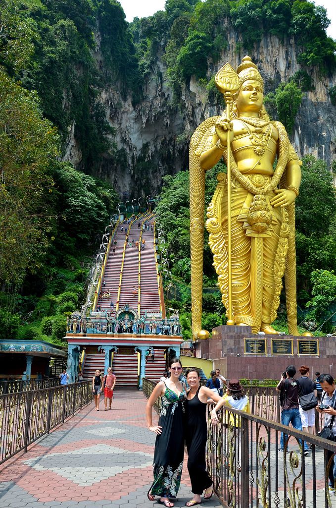 two women standing in front of a golden statue at the entrance to a cave temple