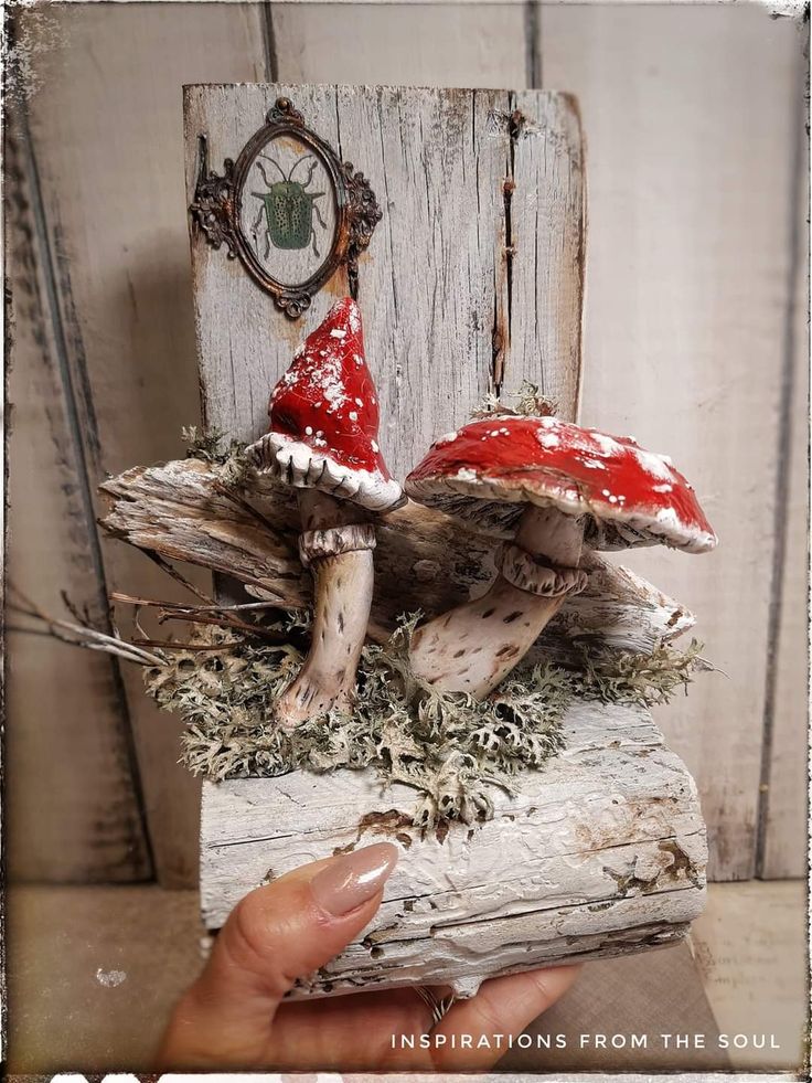 two red mushrooms sitting on top of a piece of wood with moss growing out of it