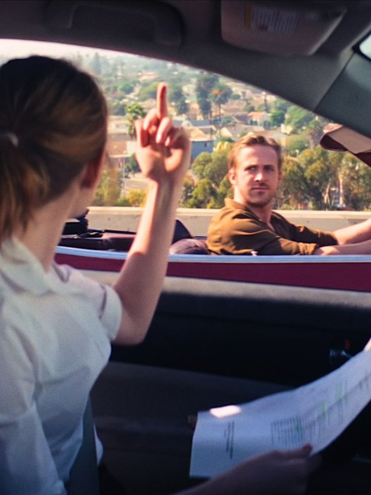 two people sitting in the back seat of a car and one person pointing at something