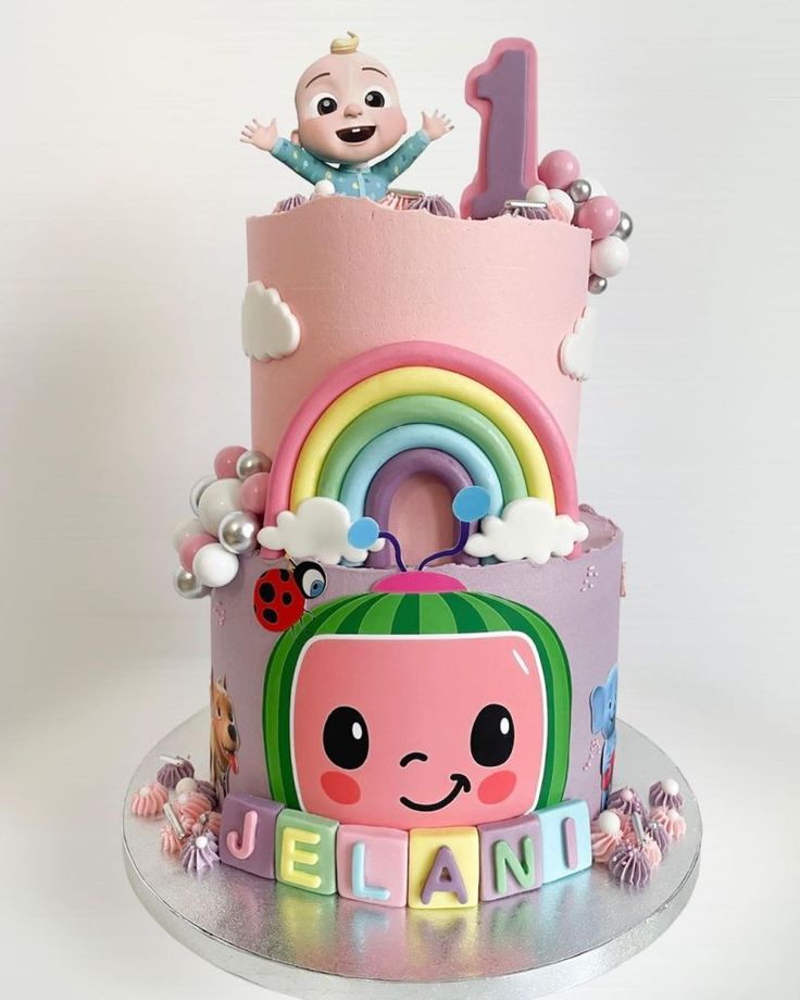 there is a pink cake decorated with animals and rainbows on the bottom tier, along with an infant's first birthday number