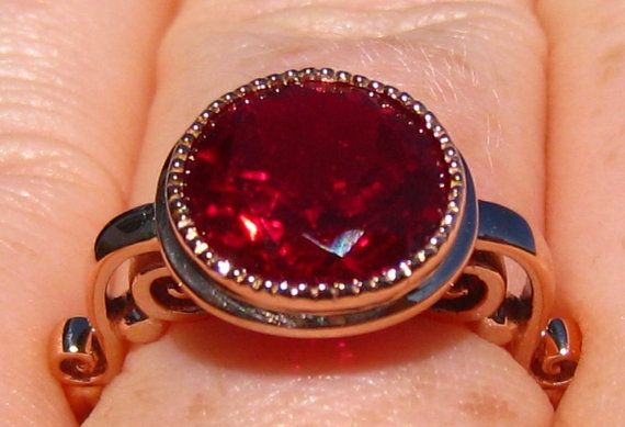 a close up of a person's hand holding a ring with a red stone