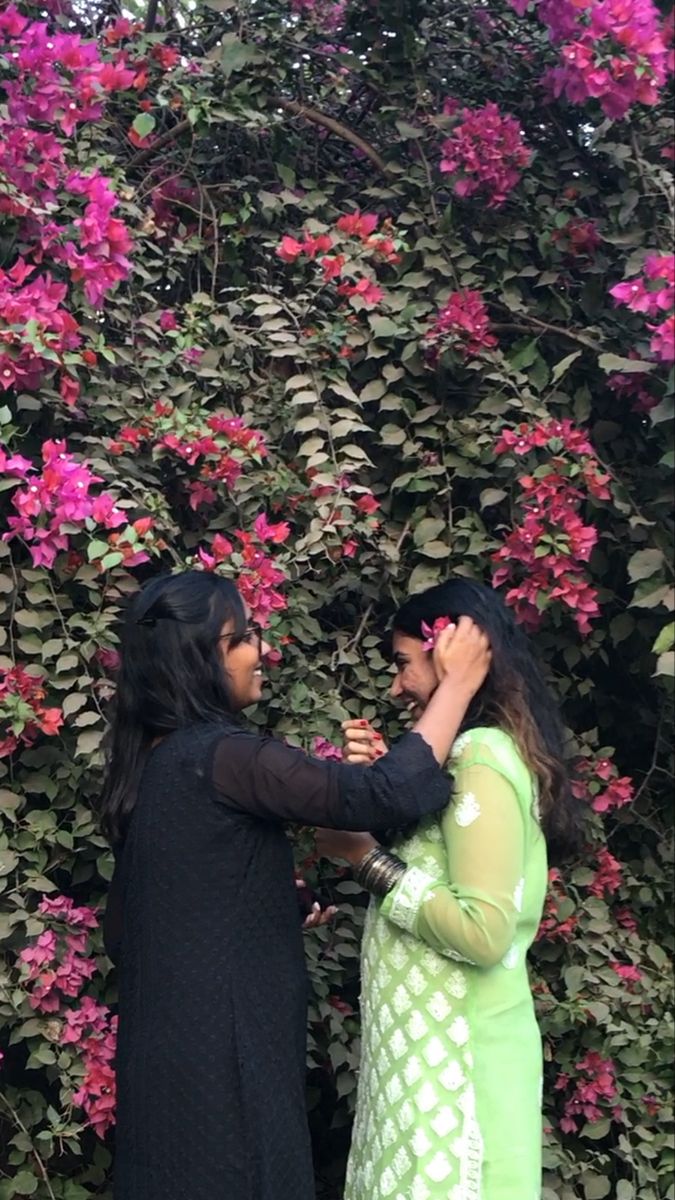 two women standing next to each other in front of pink flowers on a tree branch