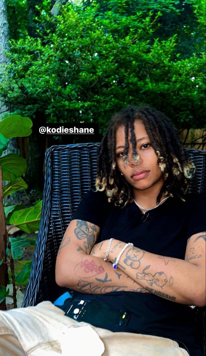 a woman sitting in a chair with her arms crossed and tattoos on her chest, looking at the camera