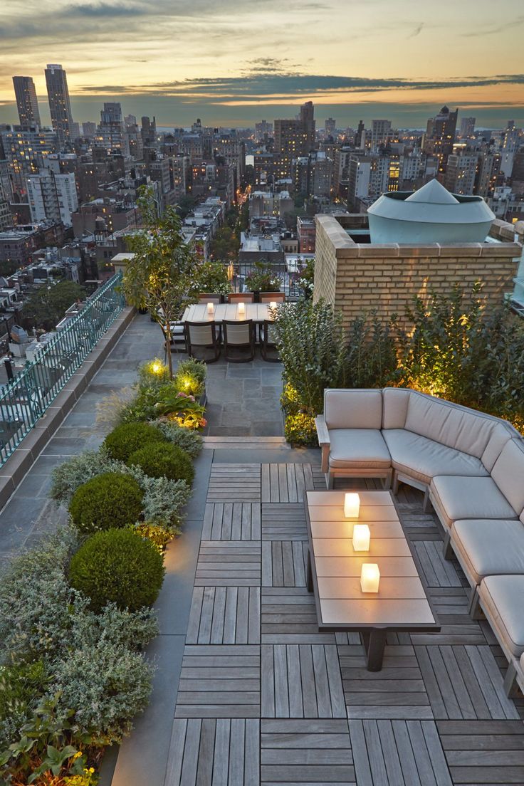 an outdoor seating area with candles lit on the tables and benches in front of cityscape