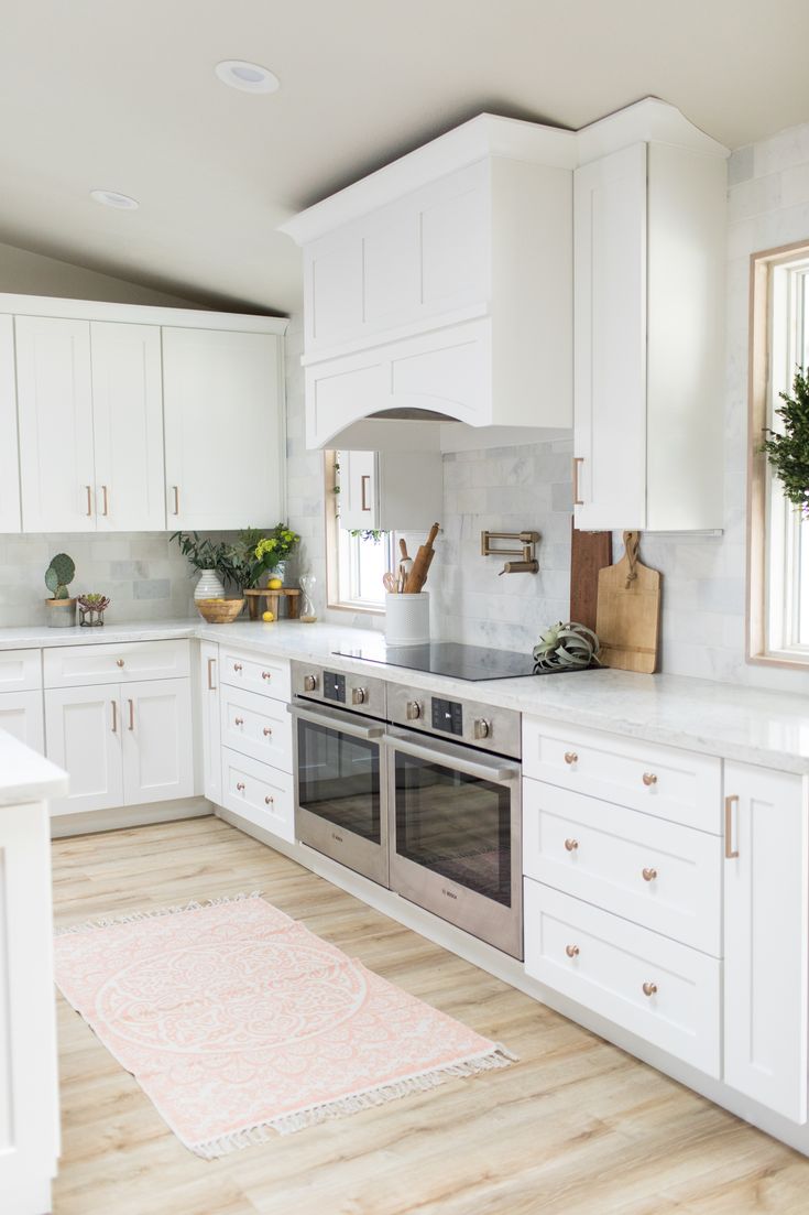 a kitchen with white cabinets and wood floors is pictured in this image, there are plants on the counter