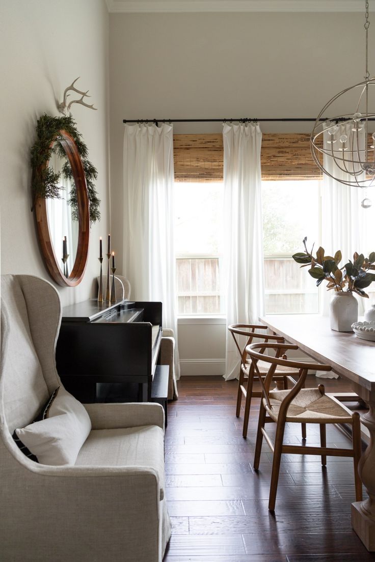 a dining room table and chairs in front of a large window with white drapes