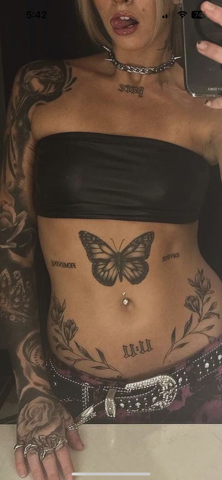 a woman with tattoos on her stomach holding a cell phone