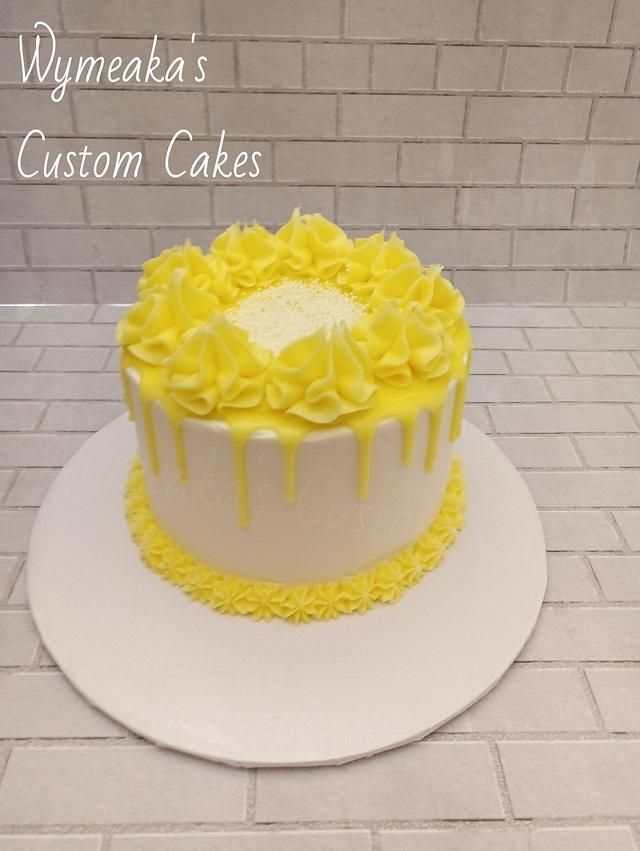 a white cake with yellow icing sitting on top of a table next to a brick wall