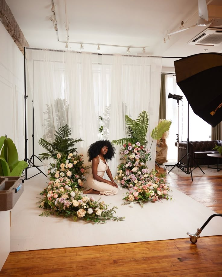 a woman sitting on the floor surrounded by flowers in front of a photo studio set up