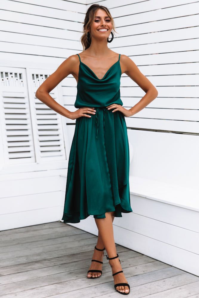 a woman in a green dress standing on a porch with her hands on her hips