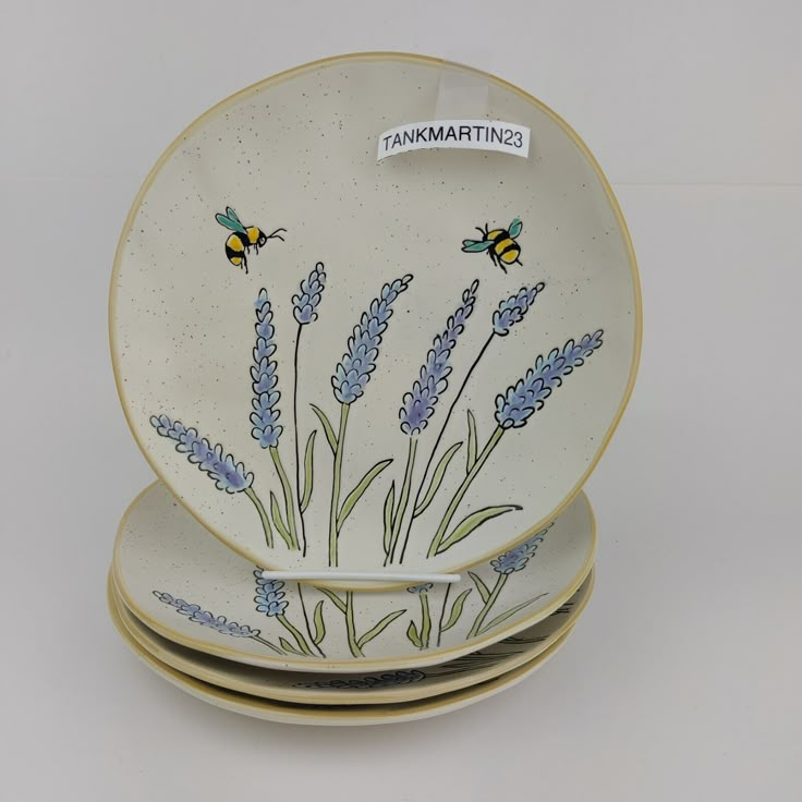 three plates with bees and lavender flowers painted on them are stacked next to each other