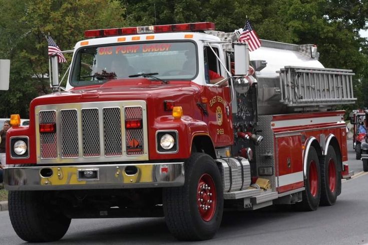 a red fire truck driving down the road with an american flag on it's side