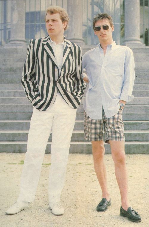 two young men standing next to each other in front of a building with stairs and steps