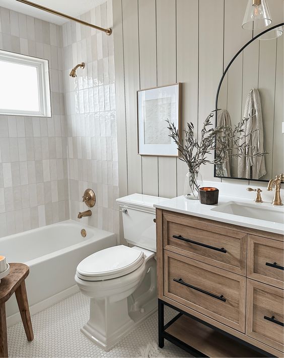 a white toilet sitting next to a bath tub in a bathroom under a mirror on top of a wooden cabinet