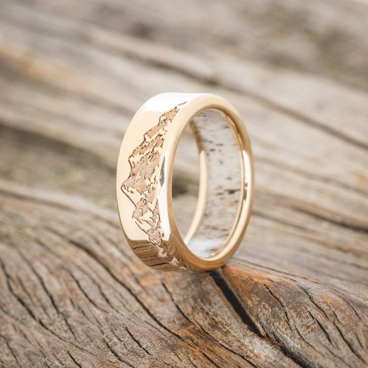 two gold wedding bands with the shape of a mountain range engraved on them sitting on a piece of wood