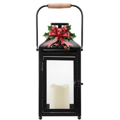 a black lantern with a red bow on it and a lit candle in front of it