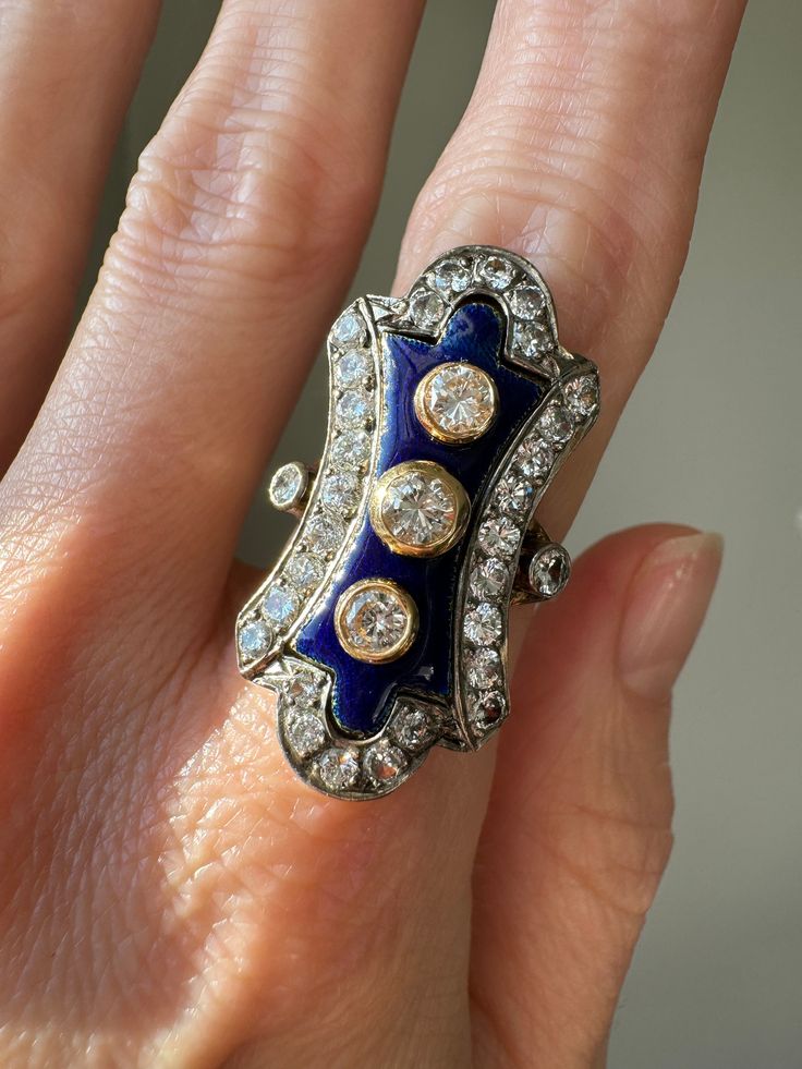 "An elegant elongated lobe-shaped ladies ring crafted in silver topped 18 karat gold featuring a center panel of blue enamel with bezel set round brilliant diamonds, surrounded by a border of round brilliant diamonds.  Measurements: 1 1/4\" long x 3/4\" wide Diamonds: approximately 2.46 total carat weight, mostly SI1  clarity, H-I-J range in color.  Size: 6.5 US Markings: partial maker's mark, import gold and silver French weevil mark and 1942 Mercury head export mark put on articles when tax was refunded in Tunisia.  Condition notes: two points of impact can be seen on the enamel, the enamel is secure and intact." Princess Ring, Ladies Ring, Silver Tops, Ring Crafts, Maker's Mark, Diamond Cluster Ring, Diamond Cluster, Brilliant Diamond, Vintage Diamond