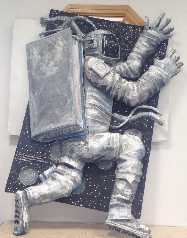 a statue of an astronaut holding a book in one hand and sitting on the other