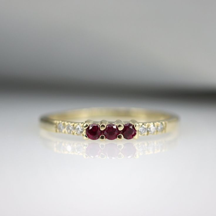 "A beautiful gemstone stacking ring, handmade in 14K Gold and set with Rubys and Diamonds. An ideal gift that is made to last a life time. Handmade by an inspired jewelry artist team with decades of experience in the craft of jewelry making. Each gemstone, each diamond is carefully picked. Using only the finest raw materials and the highest industry standard in manufacturing, design and finish. Ring Features: 3 x Natural Pink Ruby gemstones, 0.10 ct 6 x natural diamonds, 0.04 ct VS-E Ring width 14k Gold Three Stone Round Band Jewelry, Fine Jewelry Stackable Ruby Promise Ring, Ruby Stackable Promise Ring, Elegant Stackable Ruby Promise Ring, Elegant Stackable Ruby Ring For Promise, Fine Jewelry Gemstone Stackable Rings For Promise, Ruby Rings With Accent Stones In Round Band, Elegant Stackable Ruby Birthstone Ring, Ruby Rings With Accent Stones And Round Band