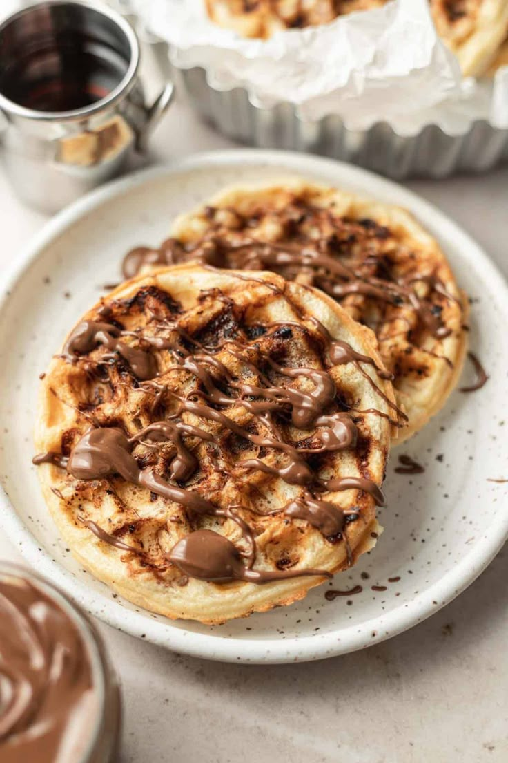 two desserts on a plate with chocolate sauce and other pastries in the background