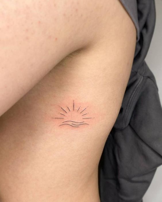 a small tattoo on the back of a woman's left arm, with sun rays coming out