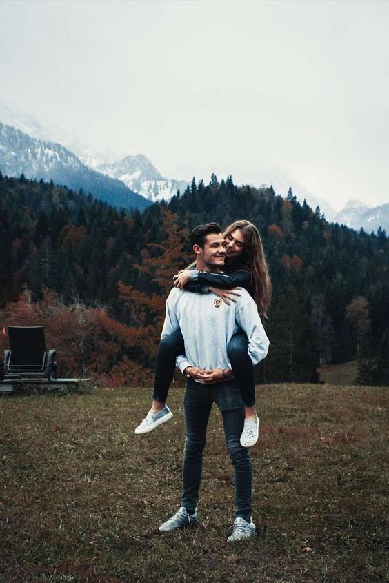 a man holding a woman in his arms while standing on top of a grass covered field