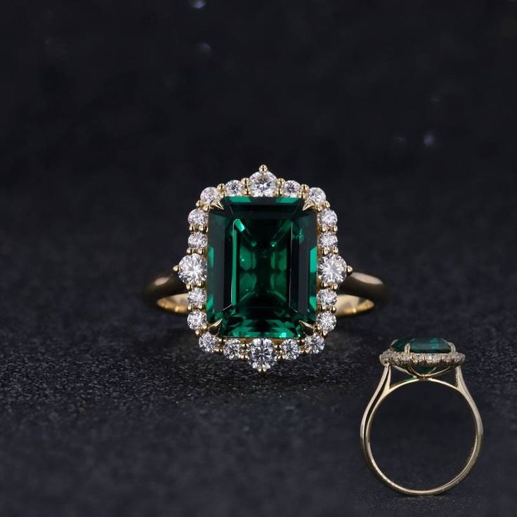 an emerald and diamond ring sitting on top of a black surface with diamonds around it