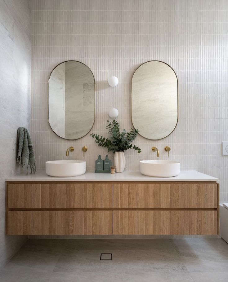 two round mirrors on the wall in a white bathroom with wooden cabinets and double sinks