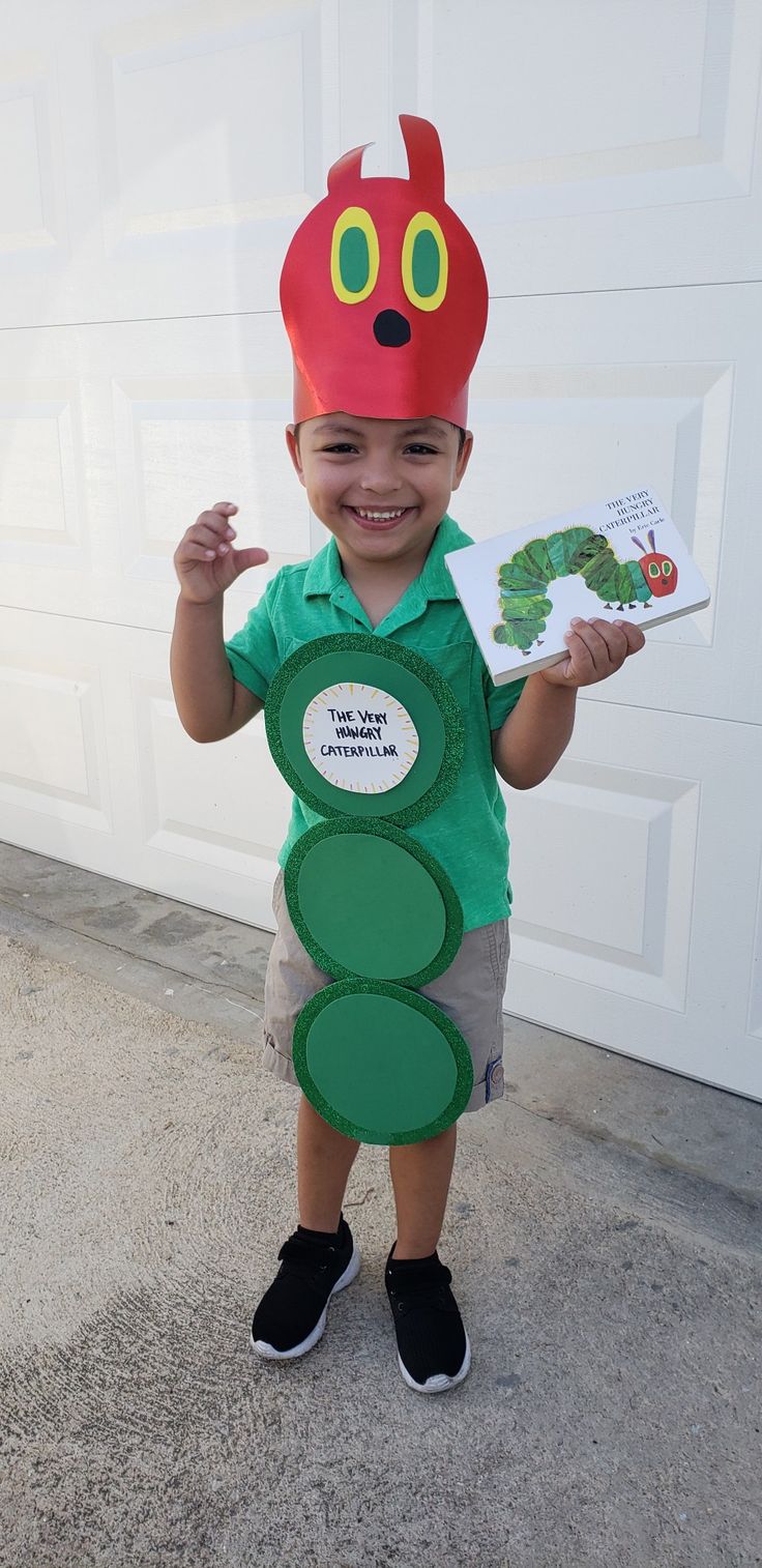 a little boy in a very cute costume holding up a paper cutout with a caterpillar on it