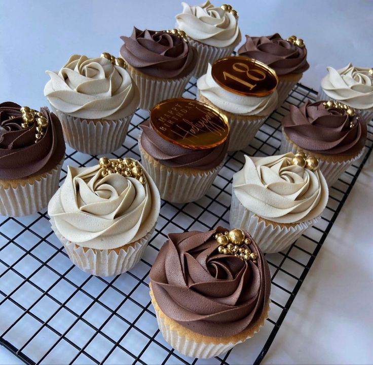 nine cupcakes with chocolate frosting and gold decorations on a cooling wire rack