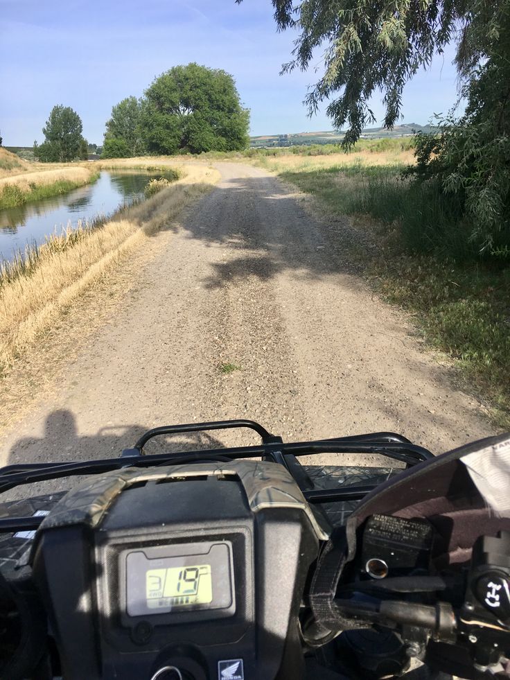 an atv driving down a dirt road next to a river