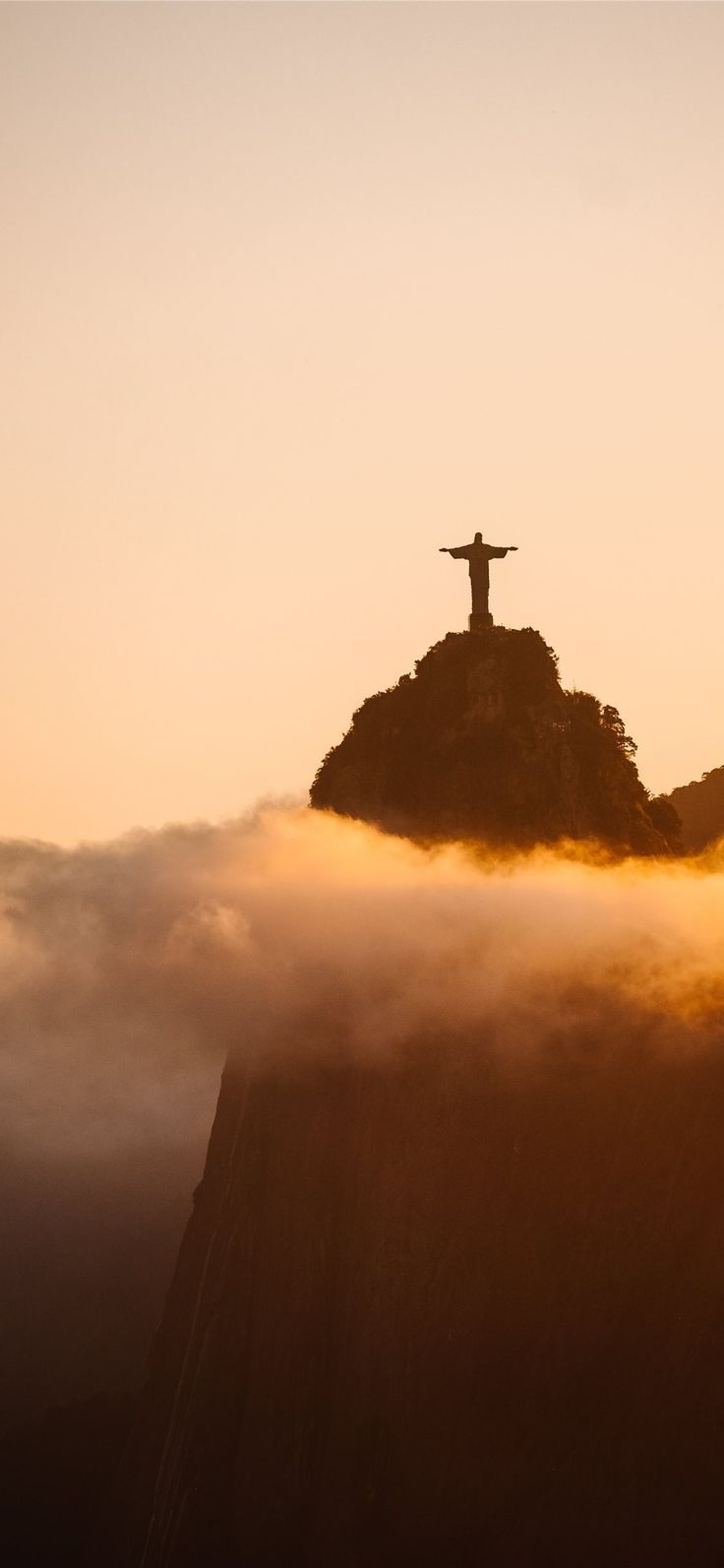 an image of the statue on top of a mountain in the sky with clouds around it