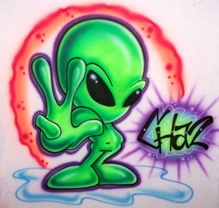 an alien is sitting on the ground in front of graffiti