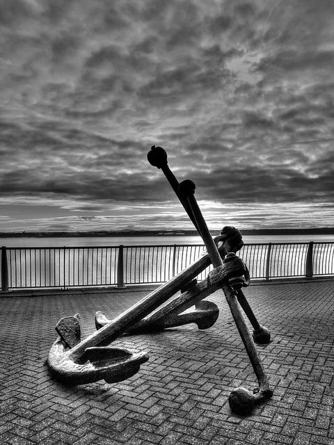 a black and white photo of an art piece on the ground in front of a body of water