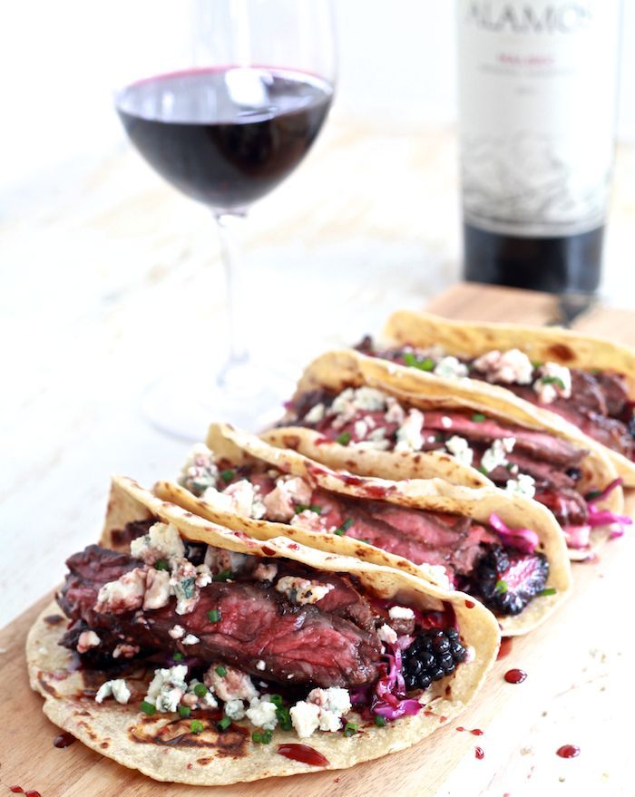 three tacos sitting on top of a cutting board next to a glass of wine