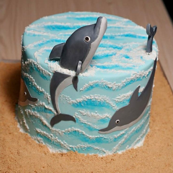 a blue cake decorated with two dolphins on the bottom and one dolphin jumping out of the water