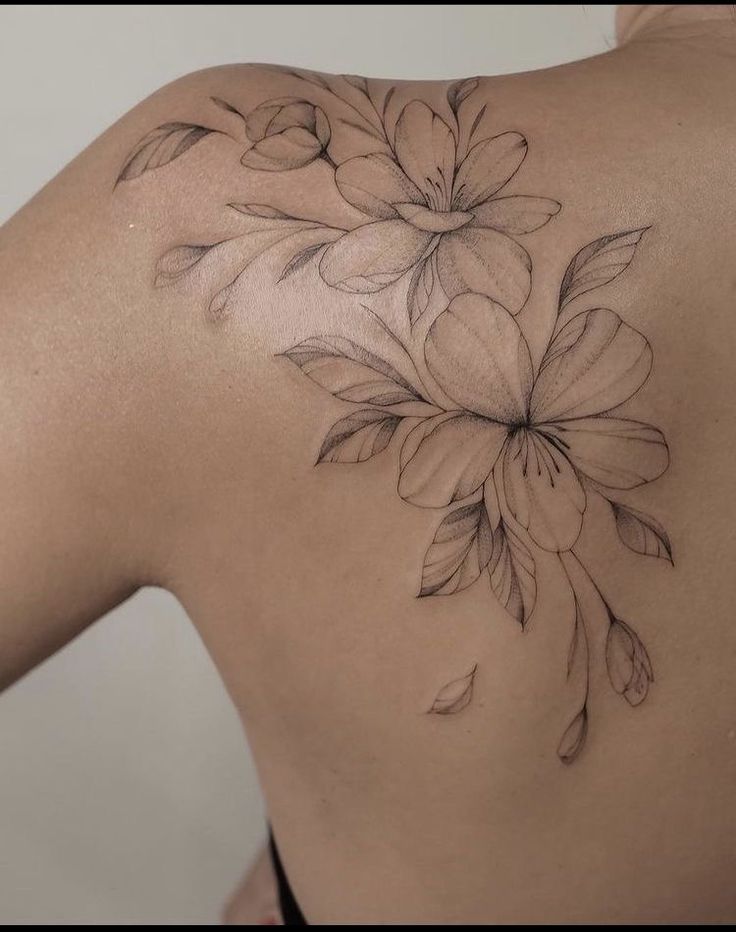 the back of a woman's shoulder with flowers tattooed on her left arm and chest