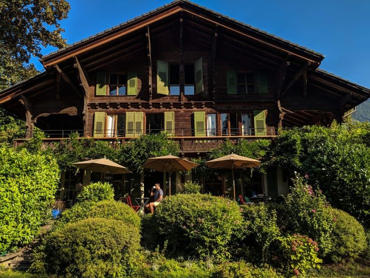 a large wooden house sitting on top of a lush green hillside next to trees and bushes